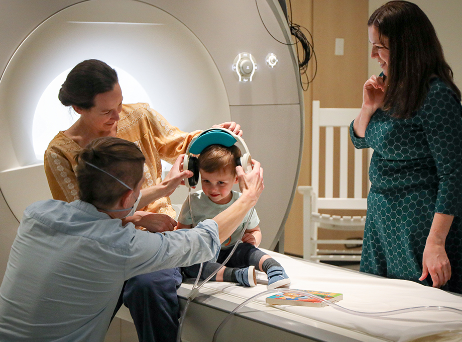 Three researchers around a toddler who is putting earphones on. OHSU researchers gain new insight on the development of binaural pitch fusion — a process that involves merging different pitches from each ear into a single sound &nbsp;— and how it affects both children with typical hearing and hearing loss. (OHSU/Christine Torres Hicks)