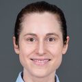 Marie Boller, M.D., has hair pulled back in a tight bun, blue shirt, and smiling.