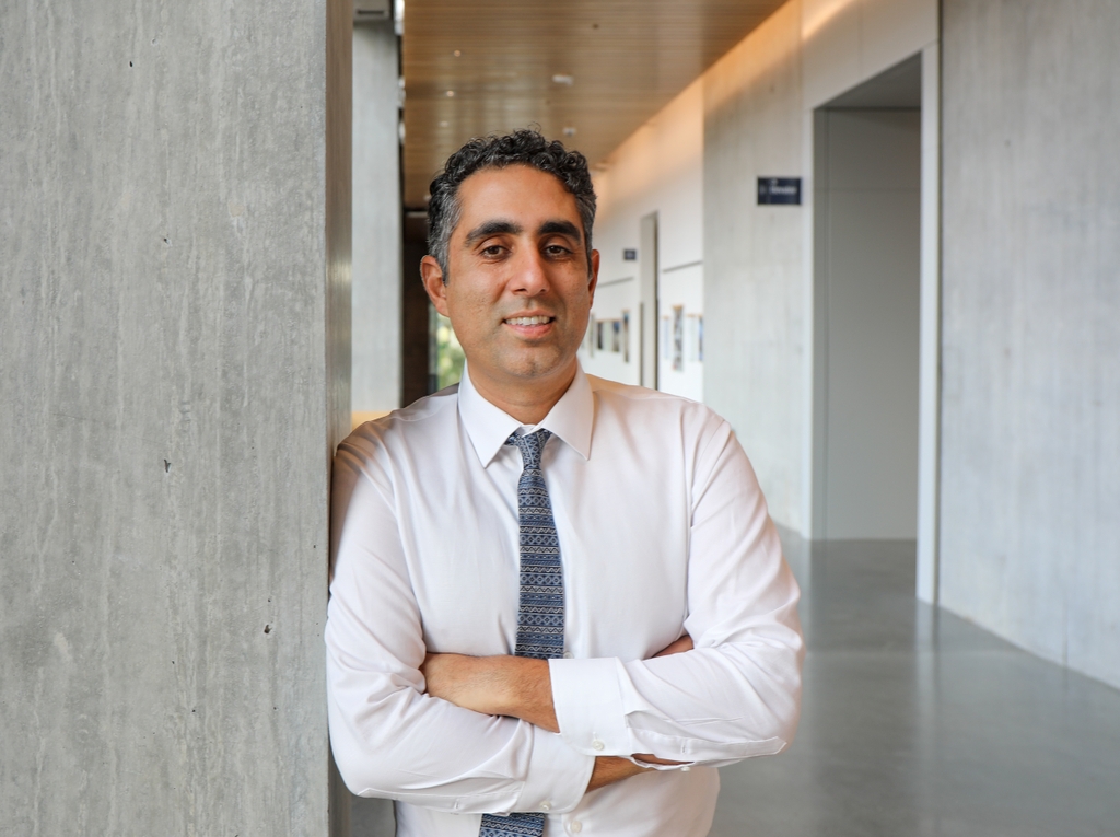 Nima Nabavizadeh, médico, tiene el pelo corto, negro y ondulado, viste camisa blanca y corbata gris, y sonríe en el Instituto del Cáncer Knight.