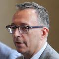 Matthias Merkel, M.D., Ph.D., has short gray/dark hair, eye glasses and a gray suit, speaking at the roundtable.