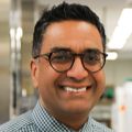 Vivek Unni, M.D., Ph.D., tiene cabello oscuro, anteojos, viste una camisa formal y corbata y está de pie sonriendo en el laboratorio.