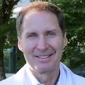 Timothy Smith, M.D., M.P.H. is tall with light brown/gray hair, blue eyes and wearing a white coat while standing in a garden at OHSU's Center for Health and Healing.