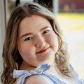 Hailey Hughes, B.S.N., tiene cabello rubio rizado y un vestido azul claro, sonriendo con la espalda contra la pared.