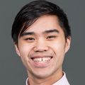 Bryan Le, Pharm. D., tiene cabello corto y oscuro, una camisa rosa y está sonriendo en un estudio fotográfico con un fondo gris.