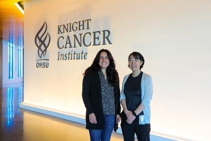Melissa Wong, Ph.D., right has short dark hair, a gray sweater and black top and pants, and Summer Gibbs, Ph.D., has long wavy dark hair, black sweater and gray top, were awarded $1,050,000 for a project titled “Noninvasive circulating hybrid cell biomarker: Early detection and monitoring of colorectal cancer.” (OHSU/Christine Torres Hicks) Image shows both standing near Knight Cancer sign.