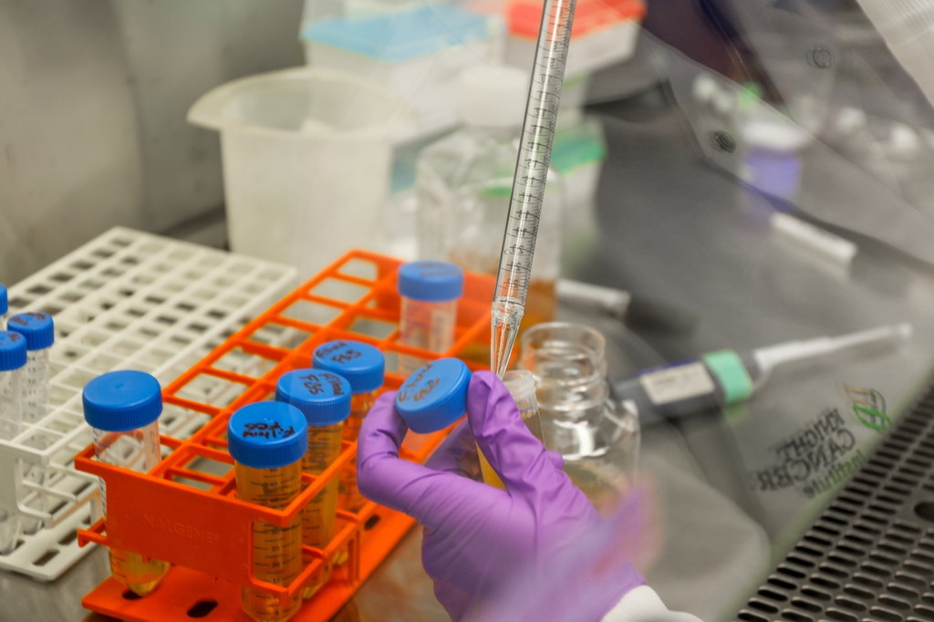 Image sows a researcher in a lab, pipetting fluids. 