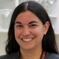 Kristin Sauter, Ph.D., tiene cabello largo, lacio y oscuro, partido en el medio, una camiseta gris y sonríe en el laboratorio.