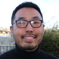 Wang tiene el pelo corto y negro, lleva gafas y un jersey negro.