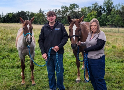 Stacey Leah Vogel of Eagle Point, Oregon, stands with her son, Jordan, and his horses, Sunny, left, and Sky. As one of the first two OHSU patients to undergo a new treatment stimulating her vagus nerve to help rehabilitate following a stroke, she's looking forward to becoming fully independent. (Courtesy) Two horses and Jordan with his mom Stacey, smiling in a grass field.
