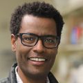 Fikadu Tafesse, Ph.D. (OHSU) Fikadu has eyeglasses, a dress shirt and vest, smiling in his lab at OHSU.