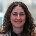 Ece Eksi, Ph.D., tiene el cabello oscuro y ondulado hasta los hombros y sonríe cerca del jumbo tron ​​de Knight Cancer en el Knight Cancer Institute.