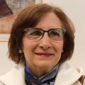 Suzanne tiene el pelo corto y oscuro, gafas y una chaqueta color crema.