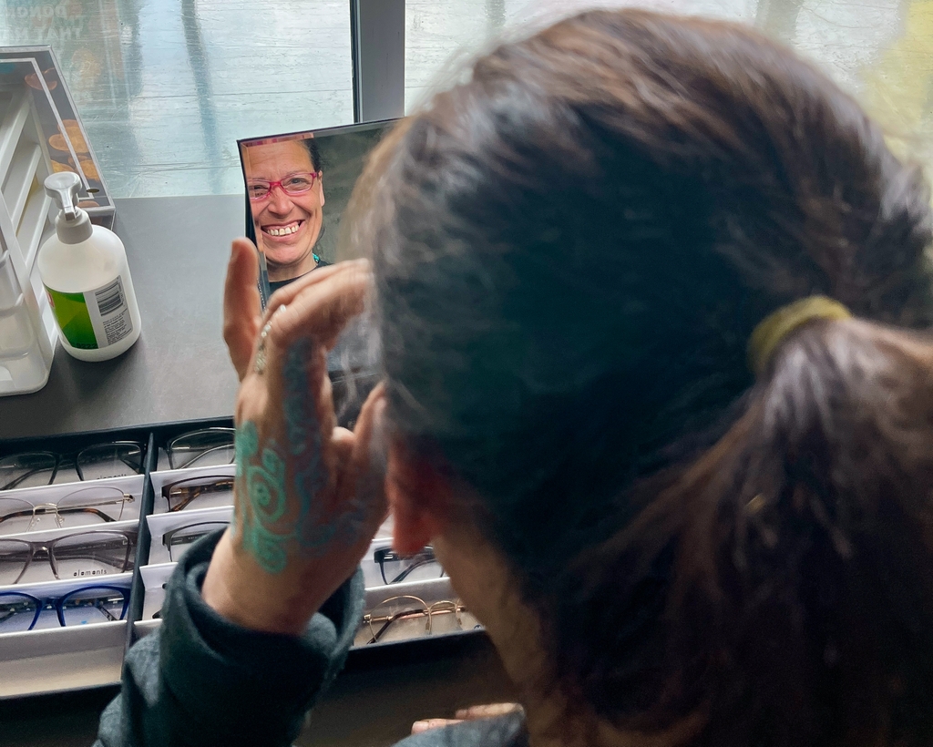 Una mujer se prueba unos anteojos nuevos y se mira en el espejo.