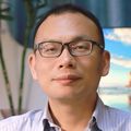 Zheng tiene el cabello corto y oscuro, gafas y una camisa de vestir, sentado frente a una computadora.