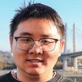 Tao tiene el cabello corto y oscuro, un suéter negro y sonríe afuera del Knight Cancer Institute en un bonito día soleado.