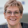 Catherine tiene cabello rubio y corto, gafas, viste un suéter gris y sonríe en el edificio Robertson Life Sciences.