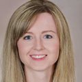 Elena has long, straight blonde hair and is smiling against a light brown photo studio backdrop.