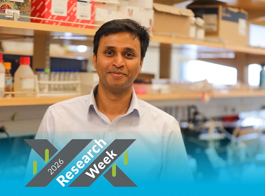 Manideep has short dark hair with a side part, a white shirt and is smiling in his lab.