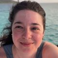 Raven has dark hair, pulled back and a gray tank top. She is aboard a boat in the water as the sun sets.