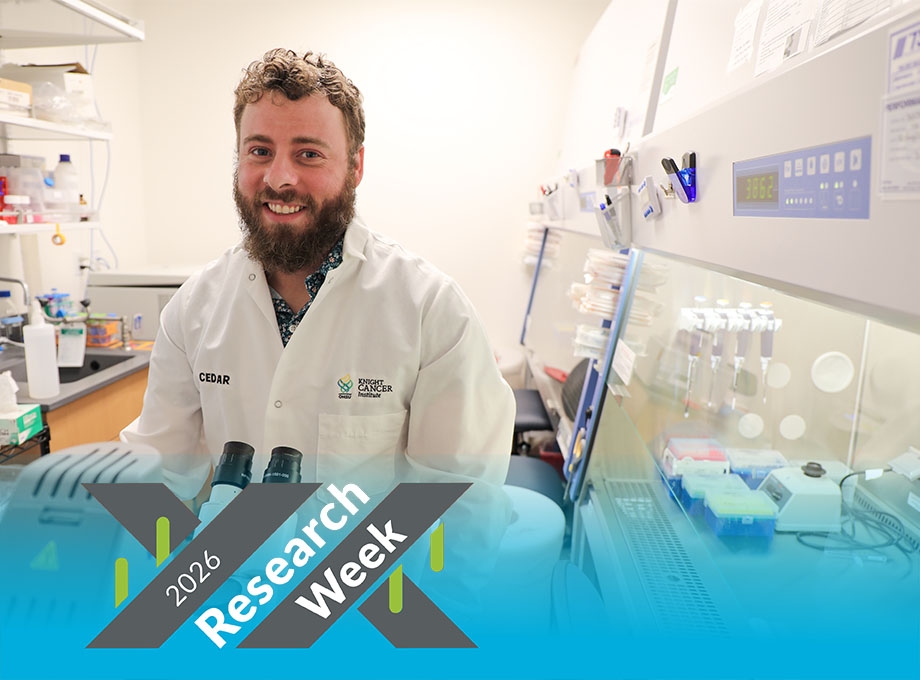 Josh has short curly, dark blond hair, wearing a white coat and smiling while at a microscope station.