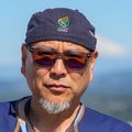Albert lleva una gorra ajustada, gafas y una bata azul, y está de pie en el helipuerto, en la parte superior del hospital OHSU.