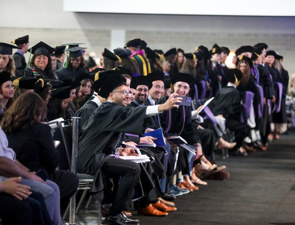 A group of graduates in the front row pose for a group selfie just before the ceremony begins.