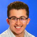 Zachary has short dark hair, eye glasses and a light-colored shirt, smiling.