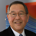 Ron has short black hair, eye glasses and a black suit with white shirt, smiling inside the School of Dentistry entryway.