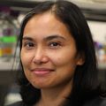 Isabelle Baconguis, Ph.D. (OHSU) Isabelle has black, straight hair to her shoulders and a black top. She is in her lab, smiling.