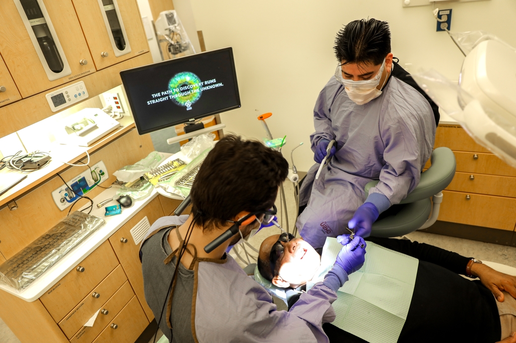 La imagen muestra a dos personas realizando un procedimiento dental a un paciente en la Facultad de Odontología de OHSU.