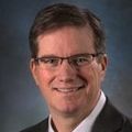 Jim has short brown hair, eye glasses and a suit.