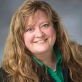 Robin has long wavy red hair and is smiling against a gray background.