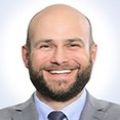 Chris has no hair, facial hair and a gray suit.