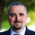 Ahmad Masri, M.D., M.S. (OHSU) Masri has very short dark gray hair, brown mustache and short goatee style beard, wearing a blue suit and blue paisley tie with a light blue dress shirt, smiling on the garden terrace at OHSU CHH1.