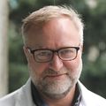 Enestvedt has short gray hair and facial hair, eye glasses and a white coat.