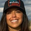 Brooke Braun (Courtesy) Brooke has long brown hair, a black baseball hat and a black shirt, smiling in a field.