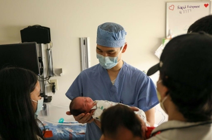 El cirujano Raphael sostiene a un bebé en una habitación del Doernbecher Children's Hospital, mientras los padres del niño(a) observan.