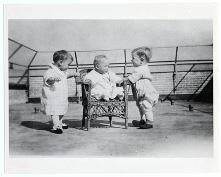 Tres niños(as) pequeños juegan en una zona de juegos cercada en Doernbecher en la década de 1930; fotografía en blanco y negro.