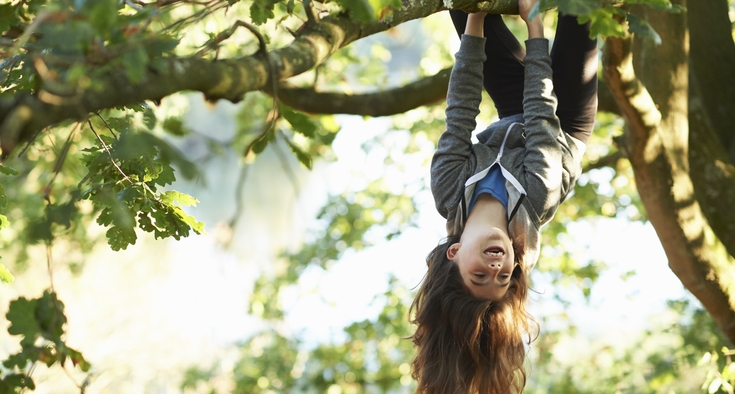 Young girl hanging upside down branch