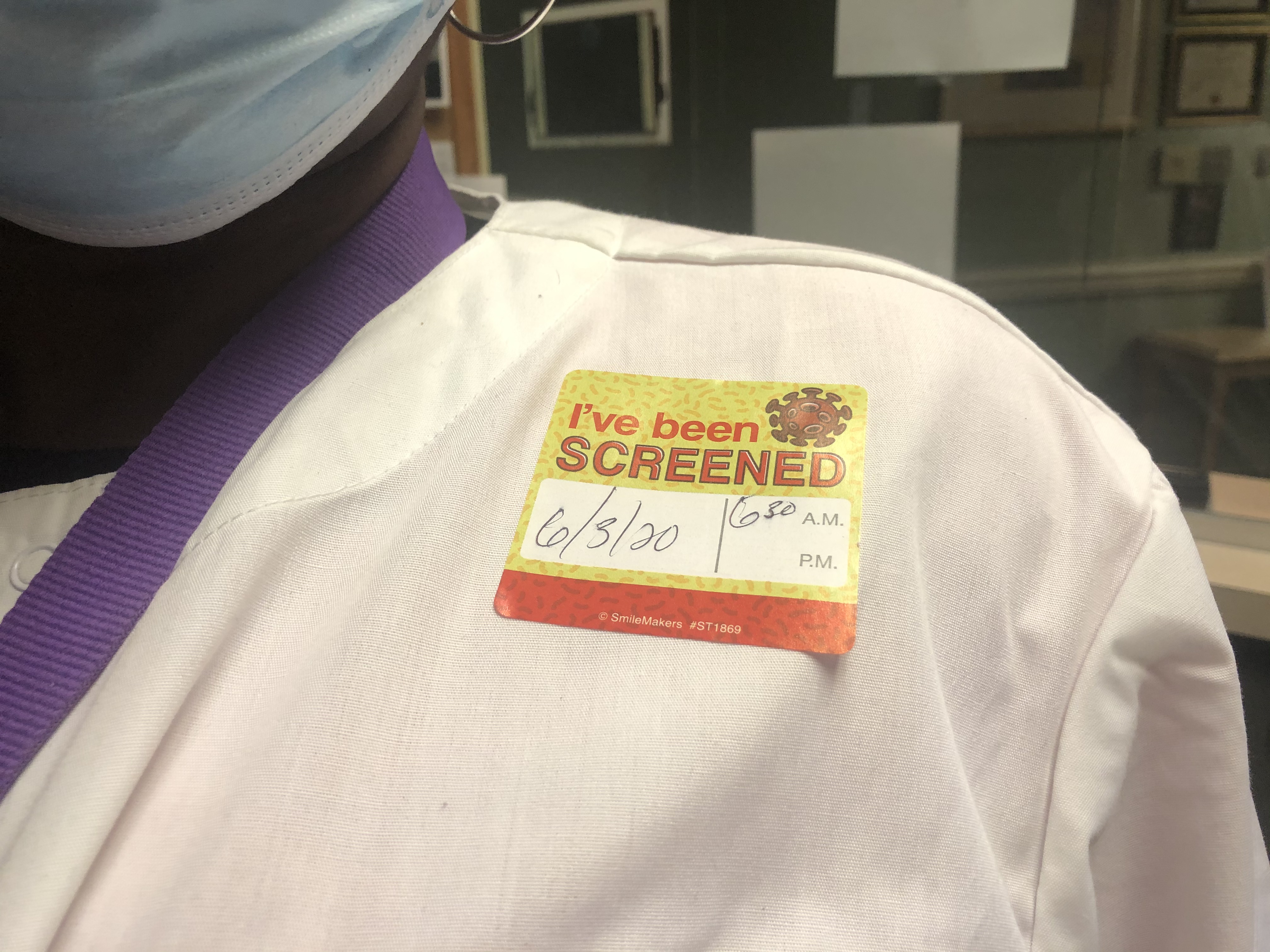 A team member wears an 'I've been screened' sticker.
