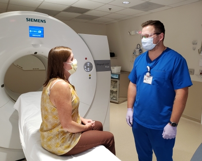 McClain is wearing a mask, standing in front of a CT scanner with a patient