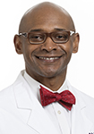 Dr. John Berry-Candelario, a Black neurosurgeon at Novant Health, smiles for a photo in a white lab coat. 