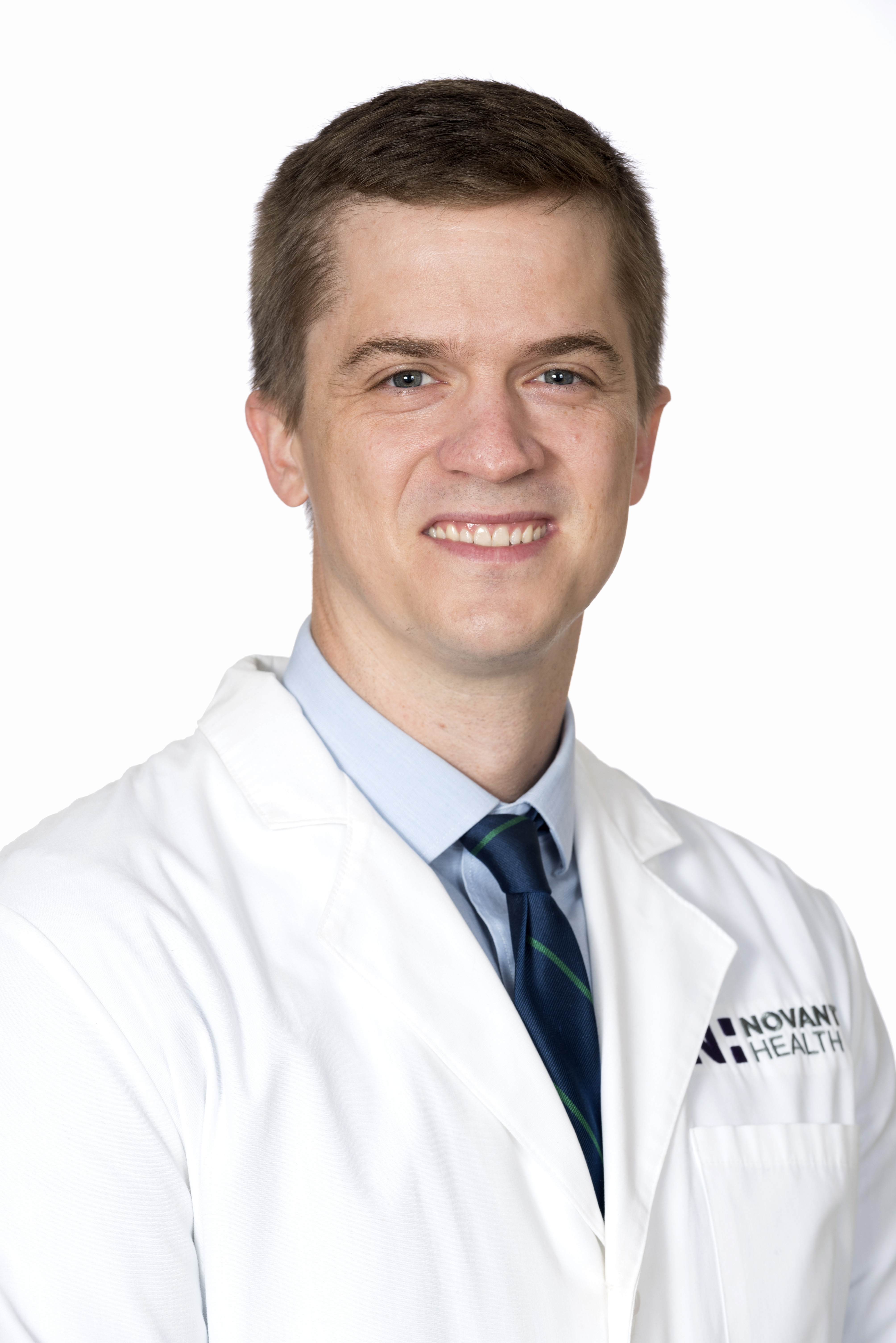Dr. Andrew Dothard, an oncologist at Novant Health Cancer Institute, smiles in a white lab coat and blue shirt.