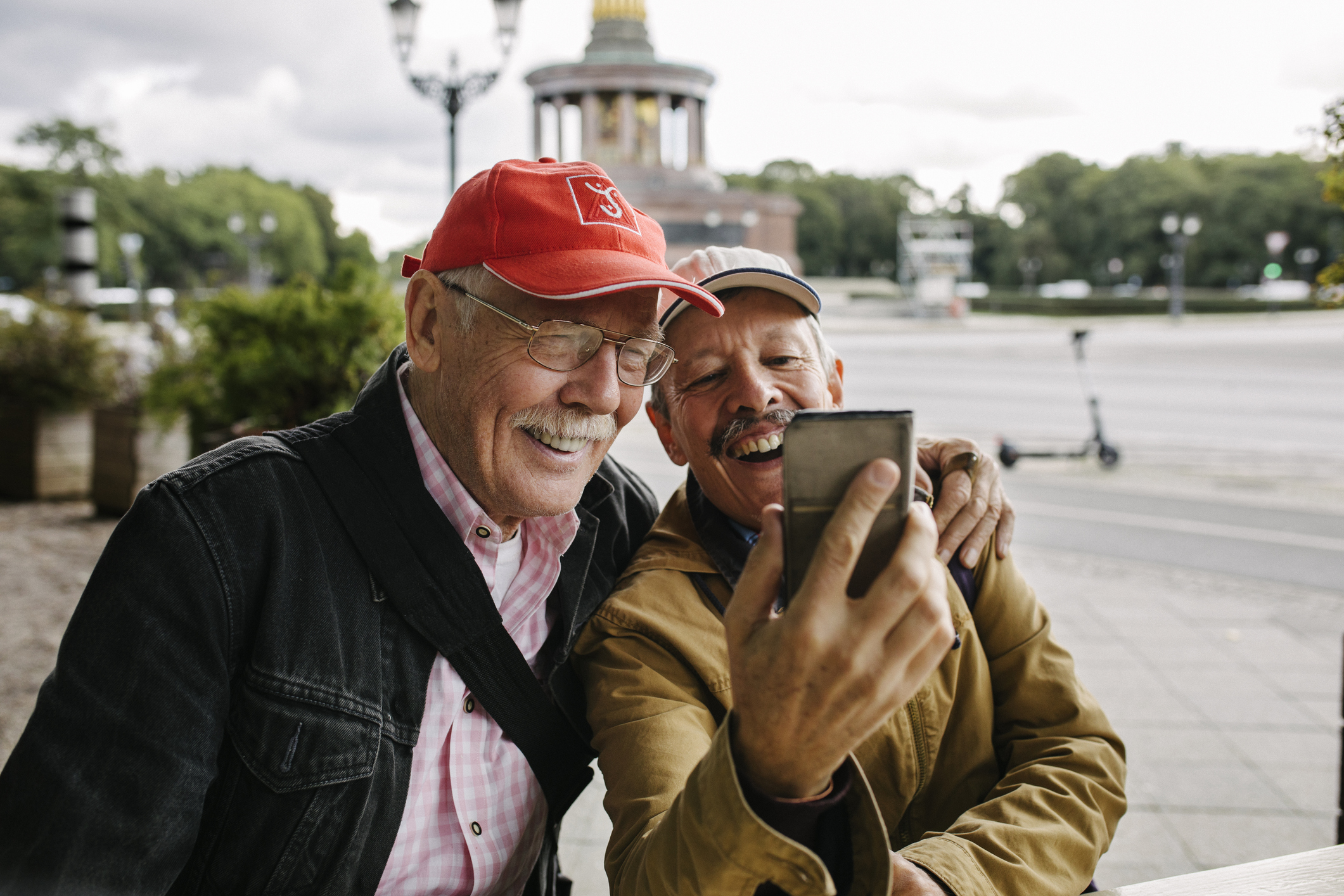 Two men laugh as they look at an image on their cell phone.