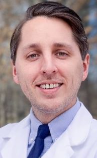 Dr. Ryan Jordanhazy smiles for a picture in a white lab coat. 