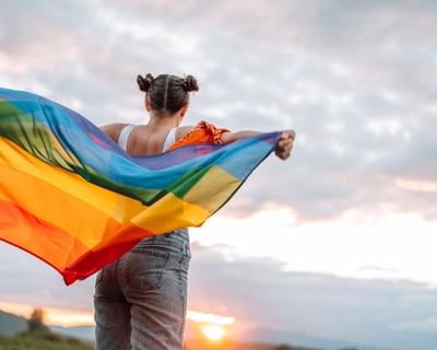 A brunette girl with pigtails looks into the sky with a bright, multicolored flag waving behind her. 