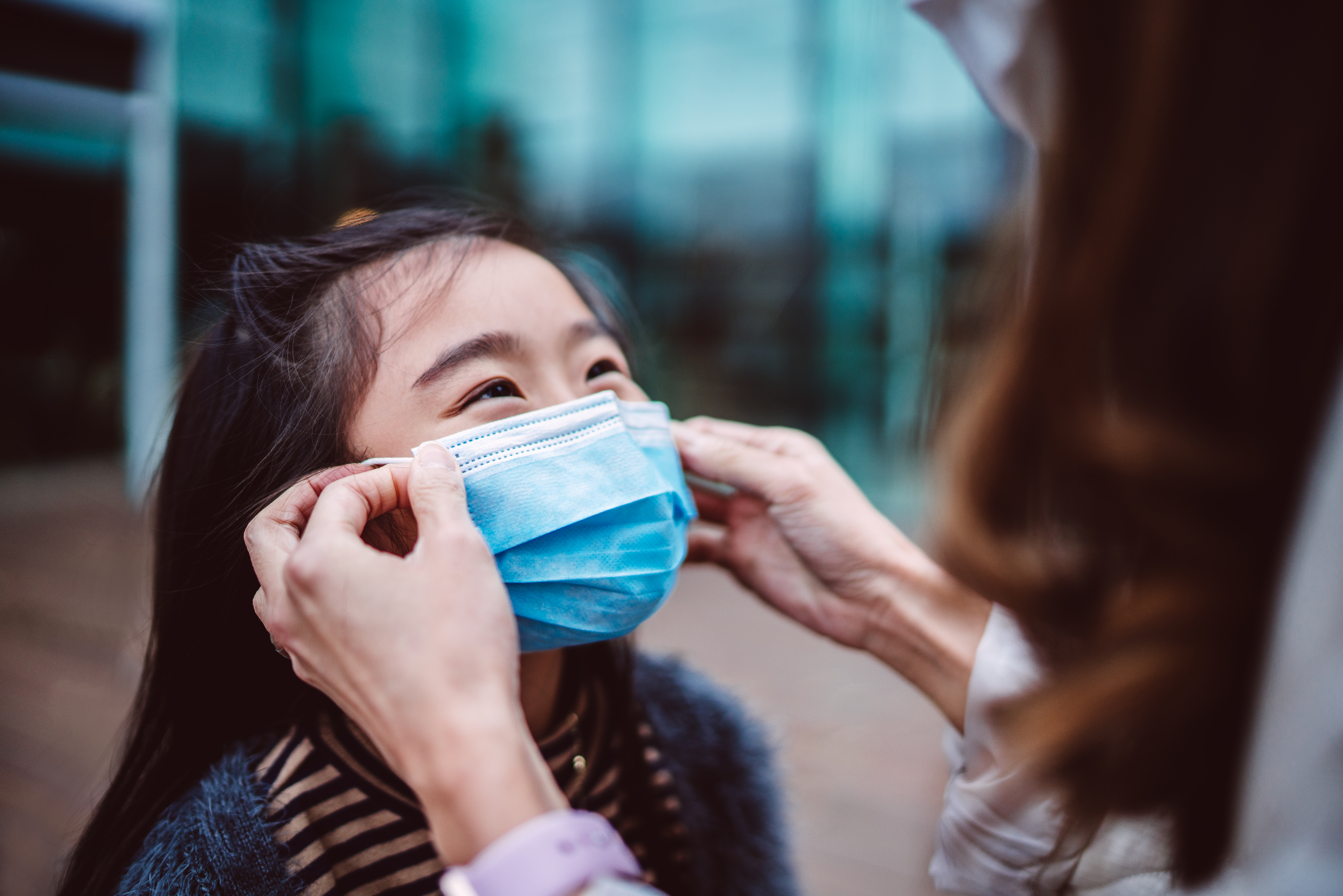 A mother helps her daughter put on a face mask.
