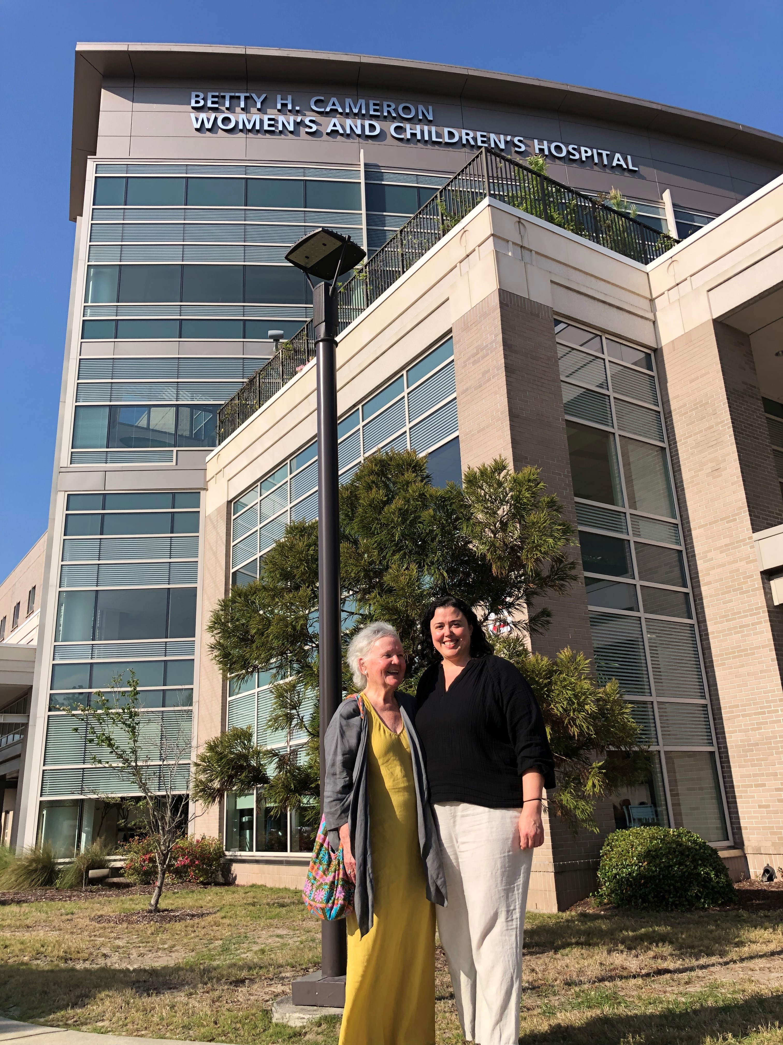 Mary Slawter and Pamela Irby stand outside of the Betty Cameron Women's and Childrens Hospital on a sunny day with a Carolina blue sky.