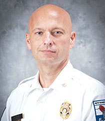 Aaron Kasulis wears a white EMS uniform shirt and smiles at the camera.