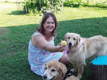 Melissa K Jones sits in the grass with her two golden retrievers